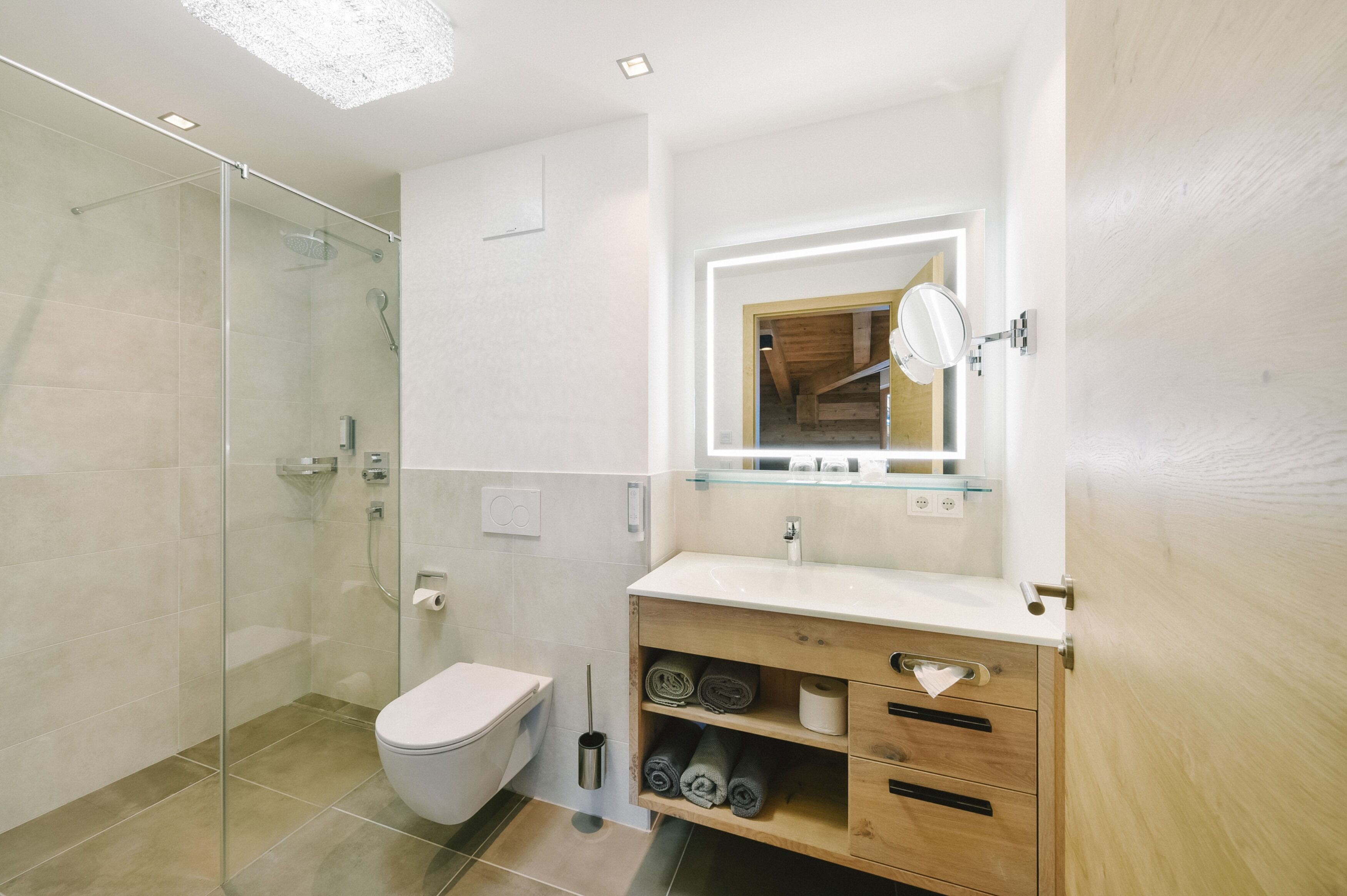 Een moderne badkamer met een douchecabine van glas, toilet, wastafel met spiegel, en netjes opgerolde handdoeken.