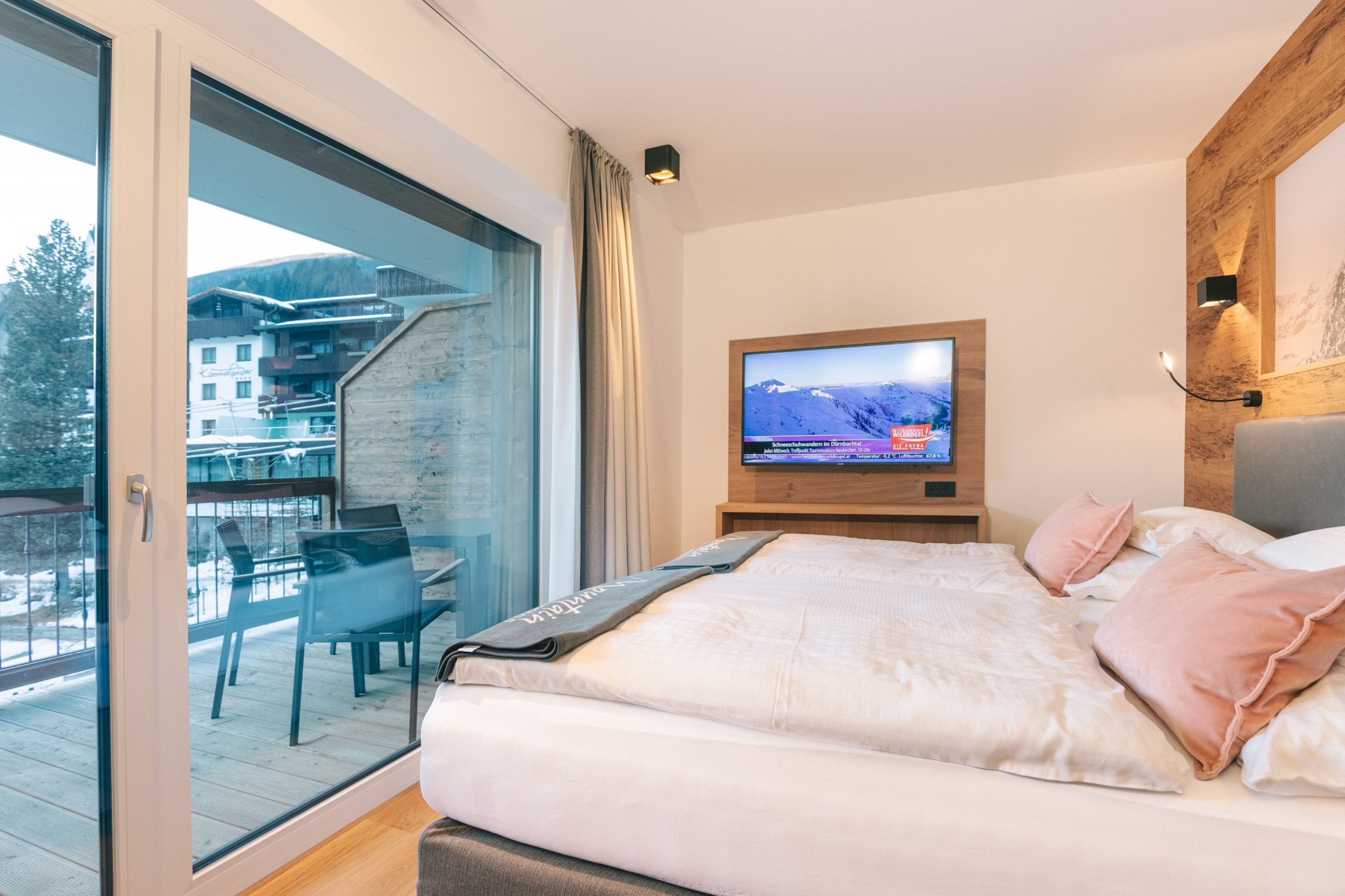 Ett modernt hotellrum med en stor säng, en tv på väggen och en balkong med utsikt över bergen.
