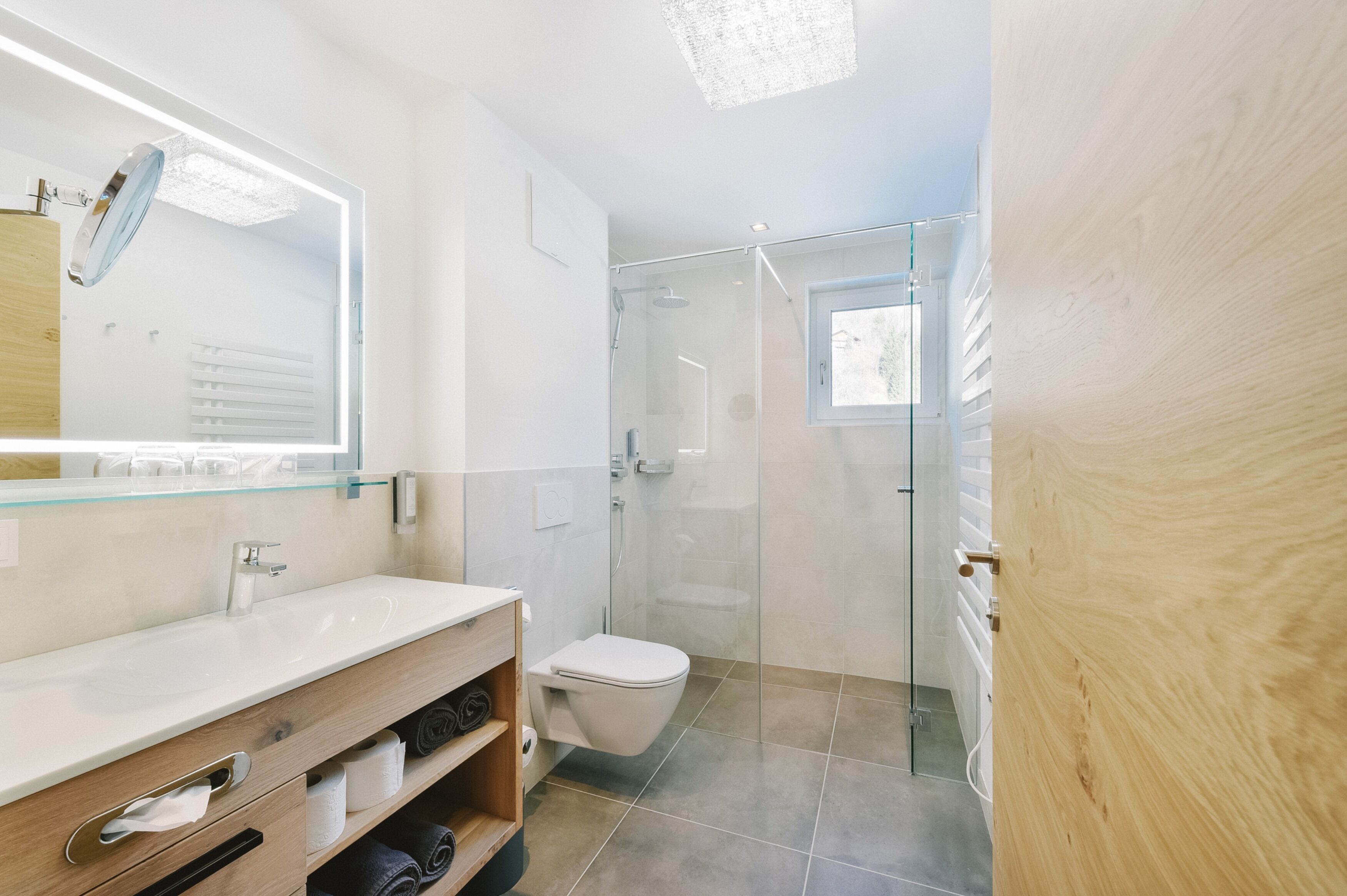 A modern bathroom with a glass shower enclosure, a wooden vanity, and a large mirror.