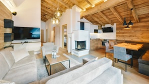 A modern living room with a large flat-screen TV, a fireplace, and a dining area with a wooden table and chairs. - Venediger Lodge (Neukirchen am Grossvenediger)