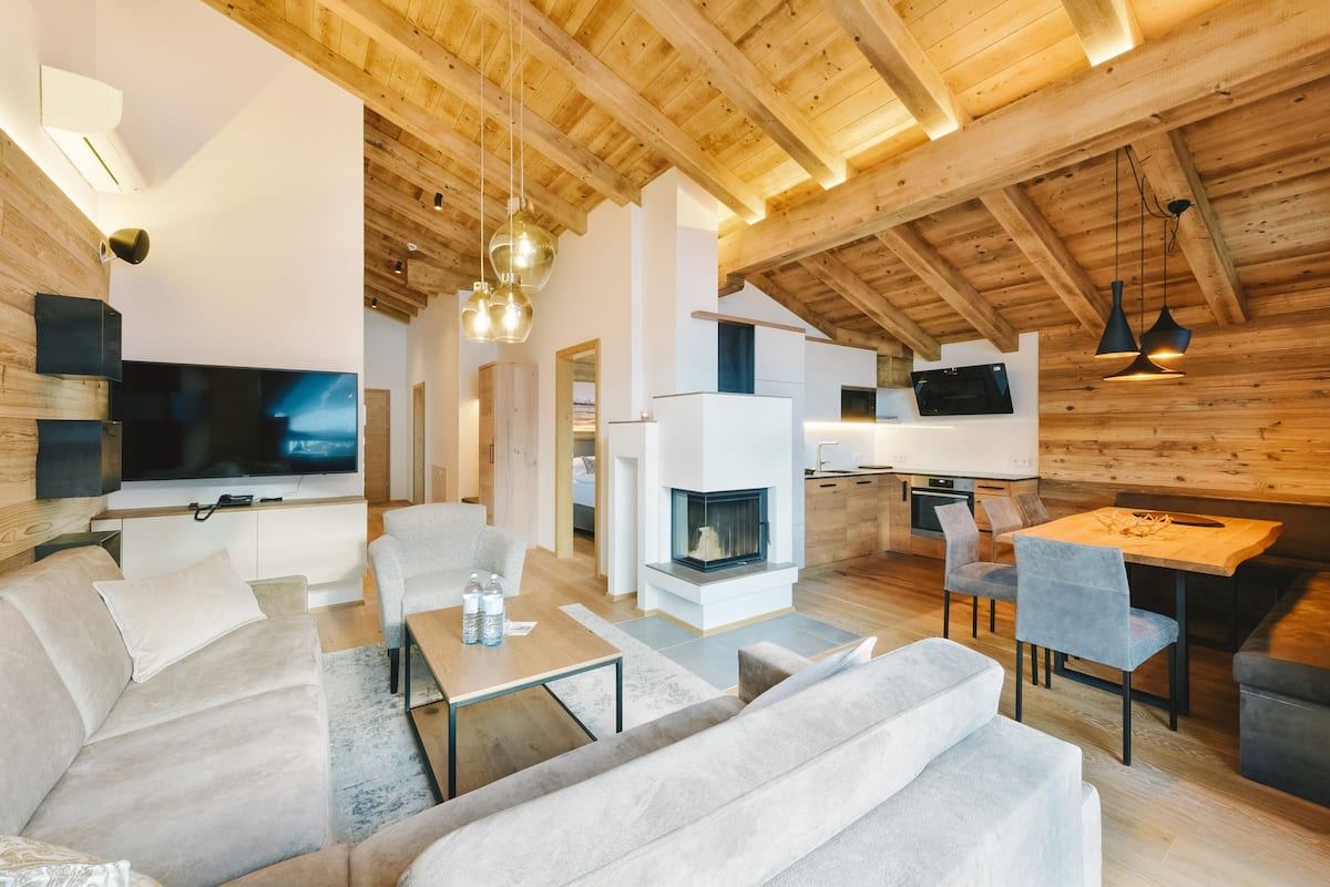 A modern living room with a large flat-screen TV, a fireplace, and a dining area with a wooden table and chairs.
