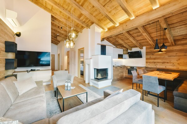 A modern living room with a large flat-screen TV, a fireplace, and a dining area with a wooden table and chairs. - Venediger Lodge (Neukirchen am Grossvenediger)