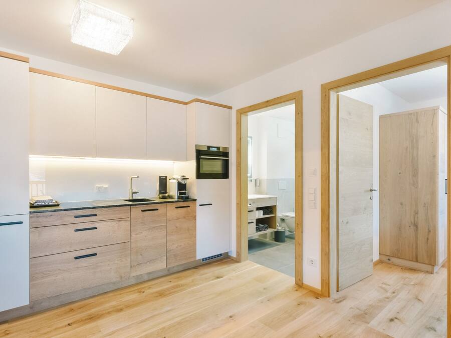 A modern kitchen with white cabinets, a built-in oven, and a countertop with a coffee machine.