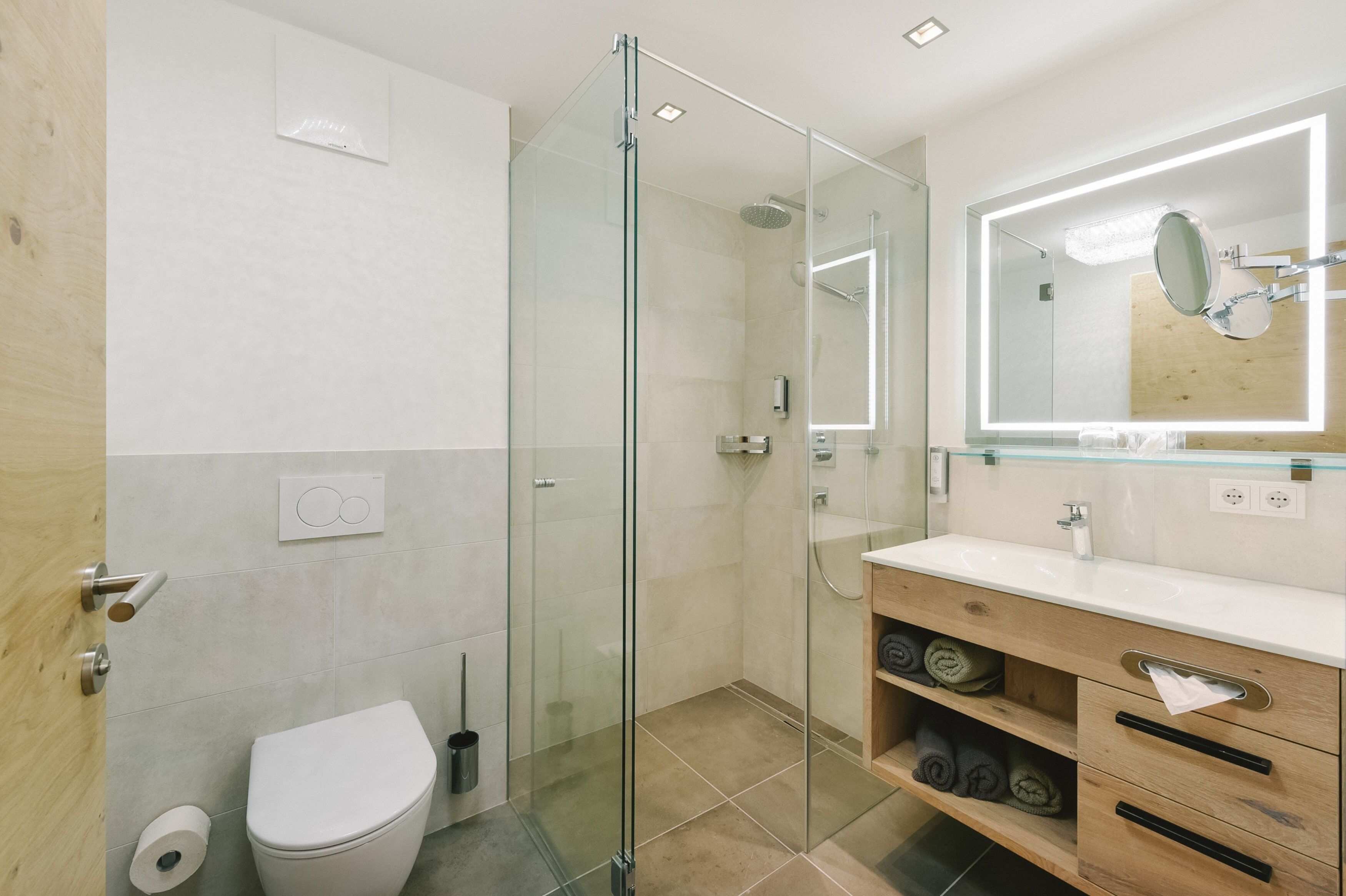 A modern bathroom with a glass-enclosed shower, a white toilet, a wooden vanity with a mirror, and a towel rack.