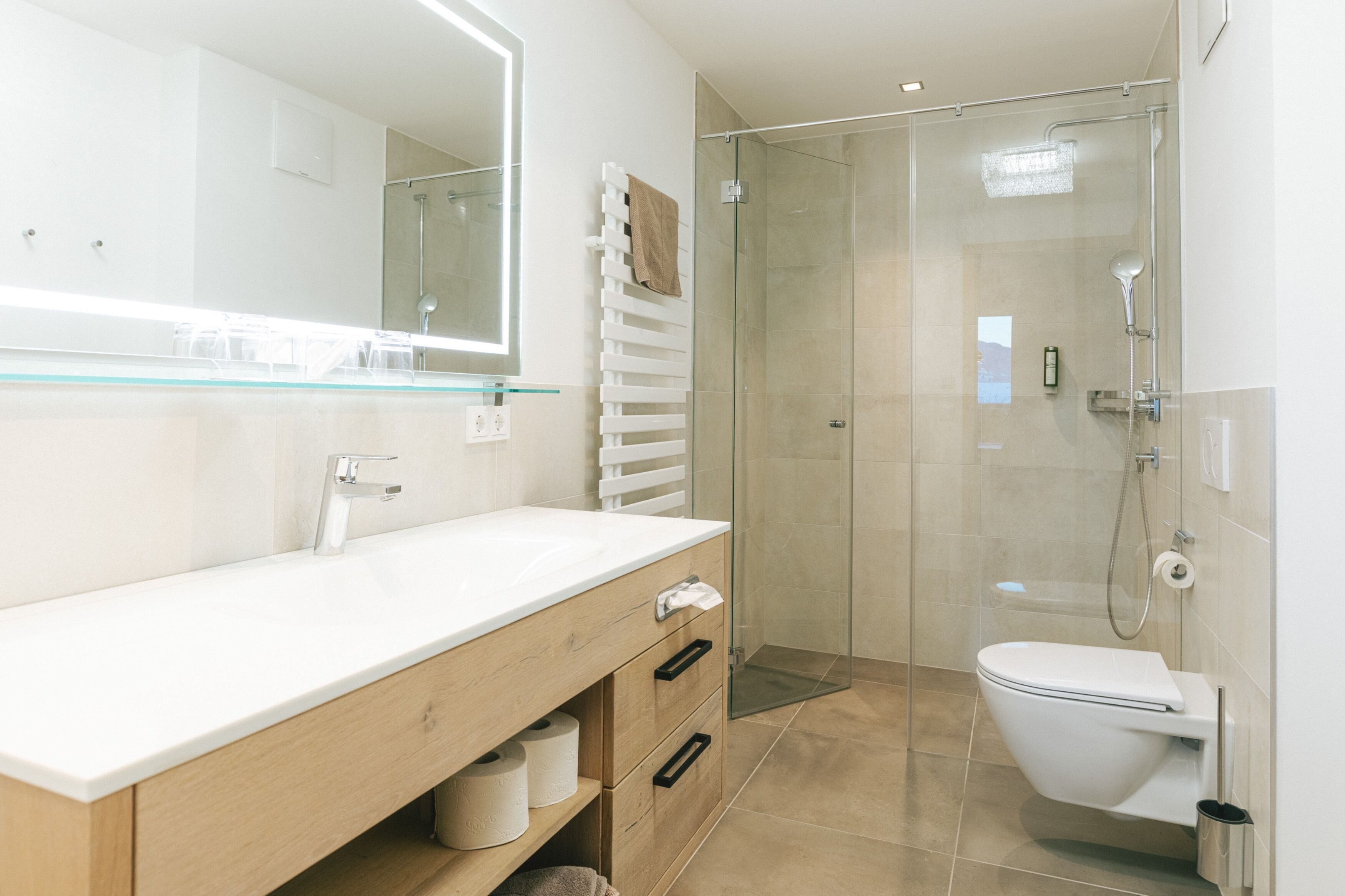 A modern bathroom with a glass-enclosed shower, a white toilet, and a wooden vanity with a mirror.