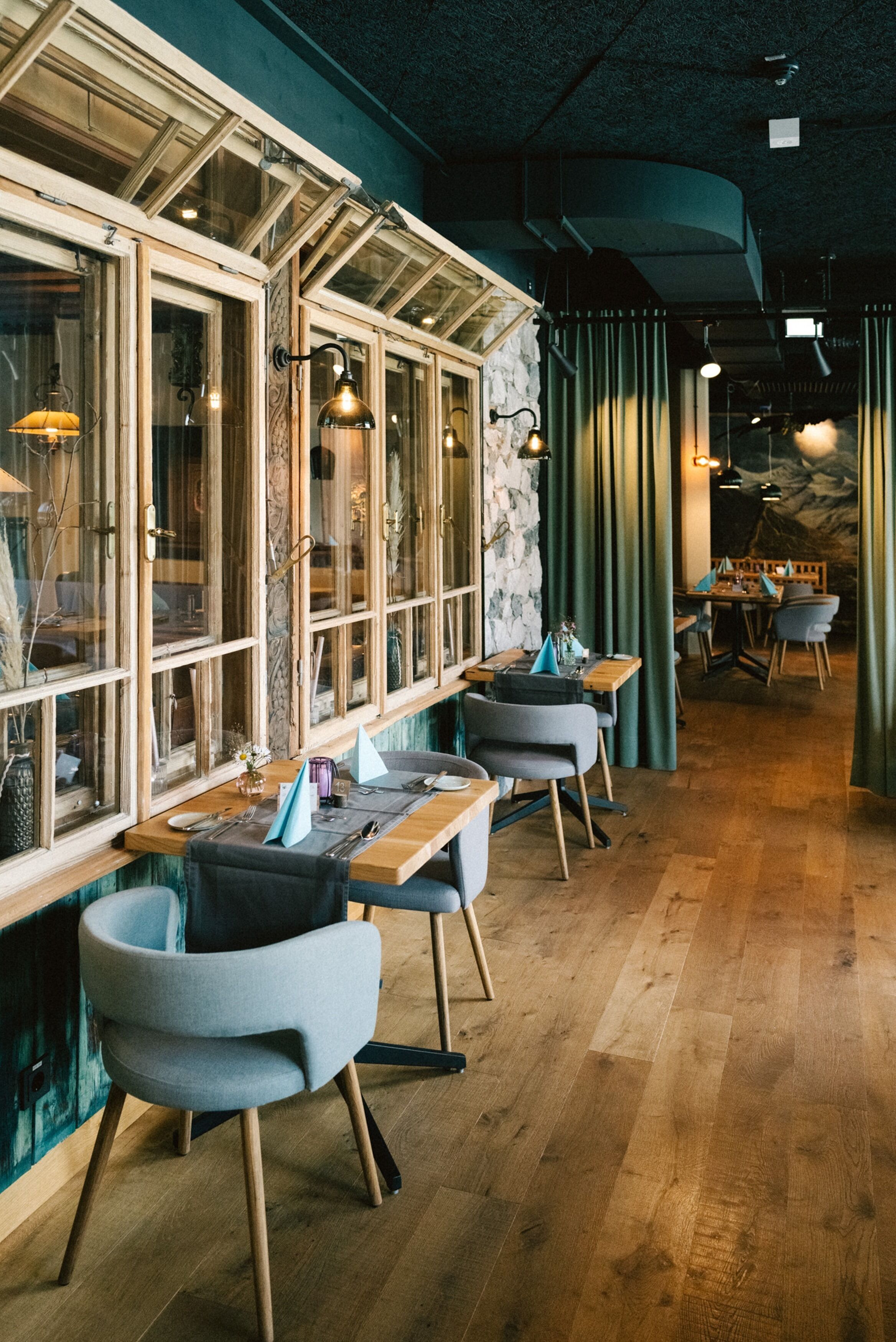 Un restaurante con mesas y sillas de madera, ventanas amplias y una pared de piedra.