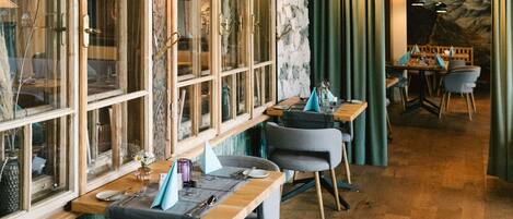 Un restaurante con mesas y sillas de madera, ventanas amplias y una pared de piedra.