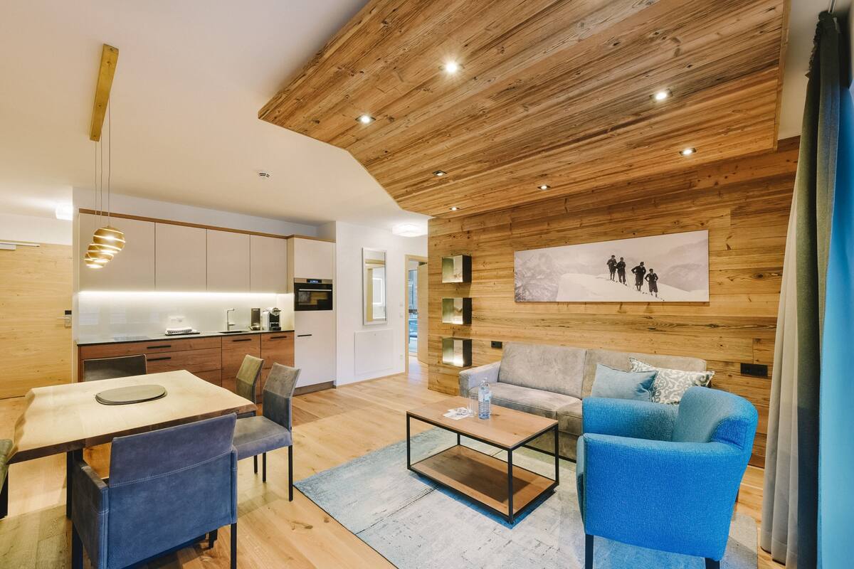 A modern living room with a wooden ceiling, a sofa, a coffee table, and a dining area with chairs.
