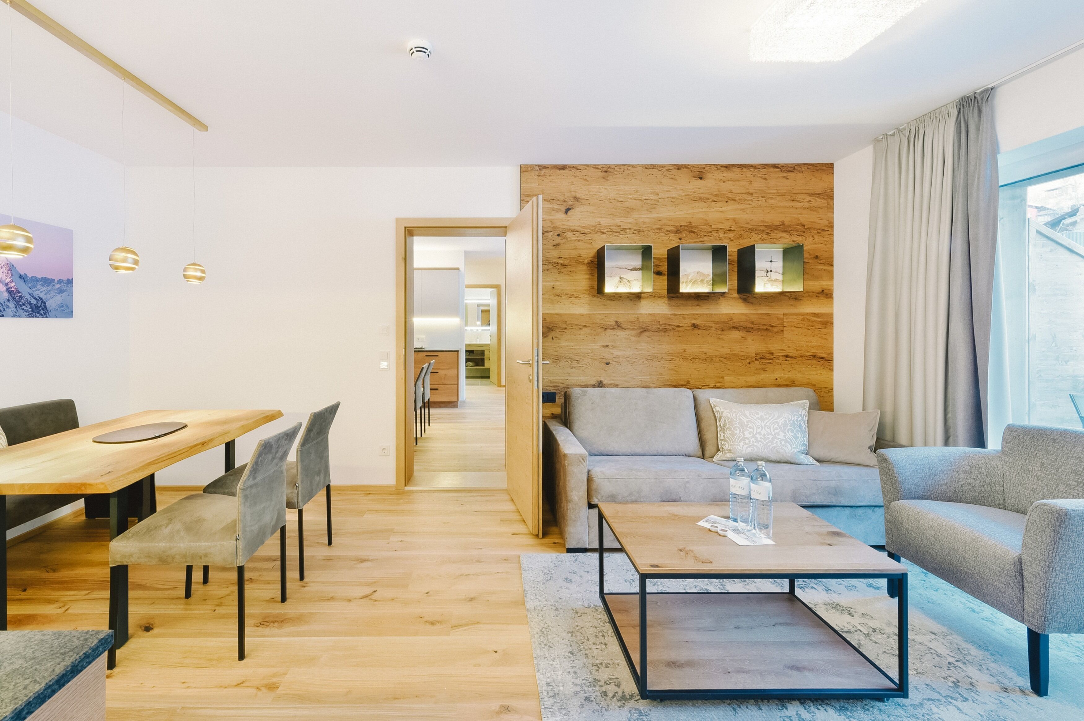 A modern living room with a wooden accent wall, a sofa, a coffee table, and a dining area with chairs and a wooden table.