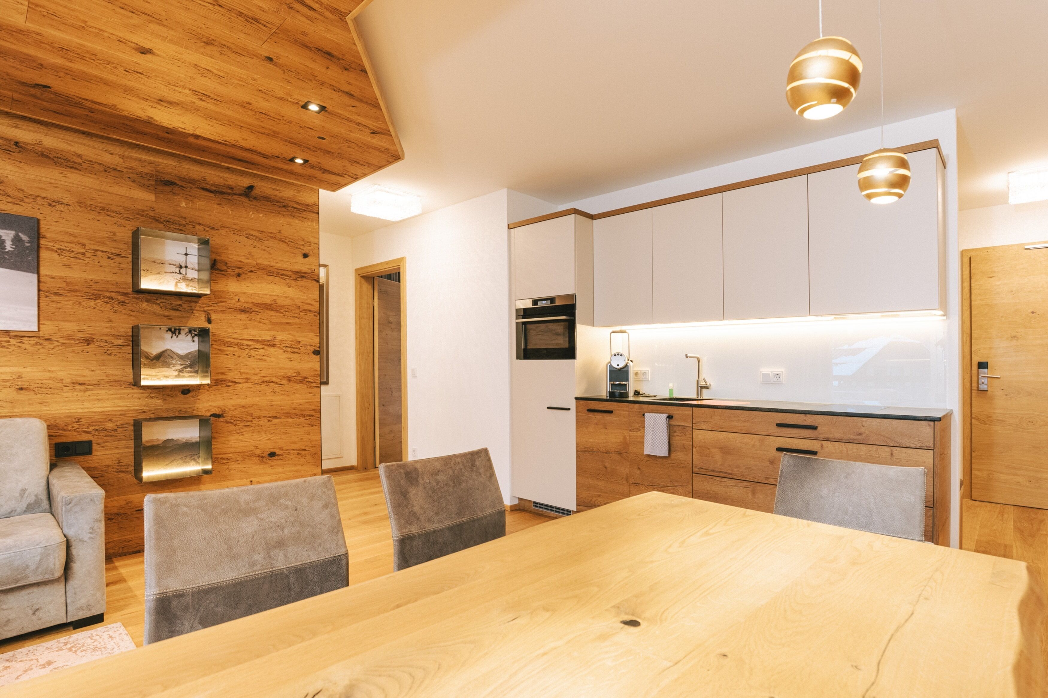 A modern kitchen with wooden cabinetry, a dining area with a wooden table and chairs, and pendant lighting.