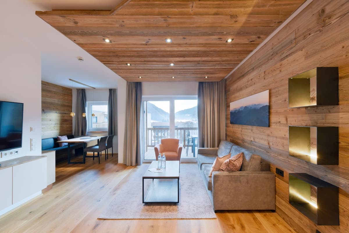 A modern living room with a wooden ceiling, a flat-screen TV, a sofa, a coffee table, and a dining area with a table and chairs.