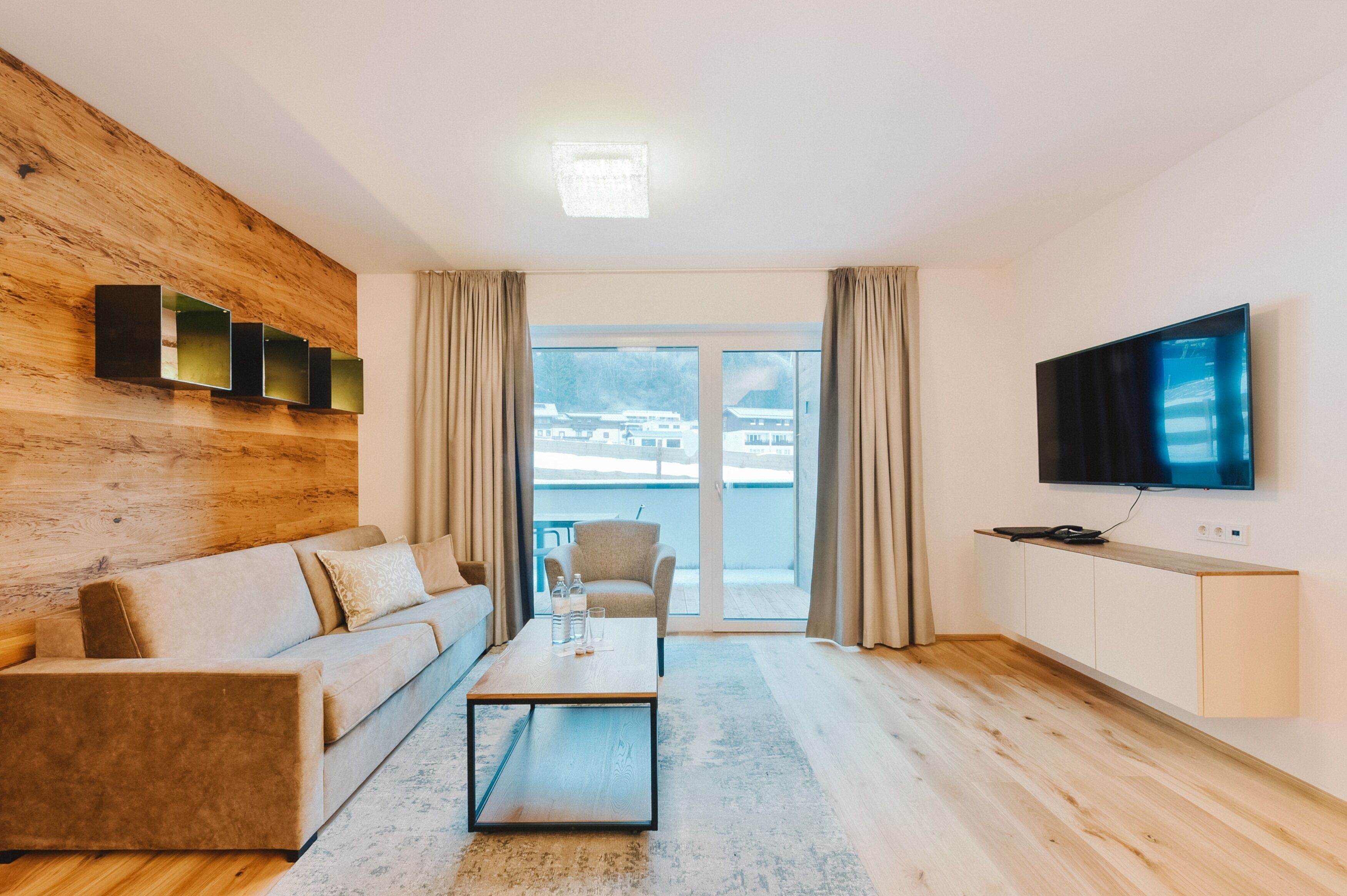 Un salon moderne avec un mur d’accent en bois, un canapé, une table basse, un téléviseur et une vue à travers une porte vitrée.