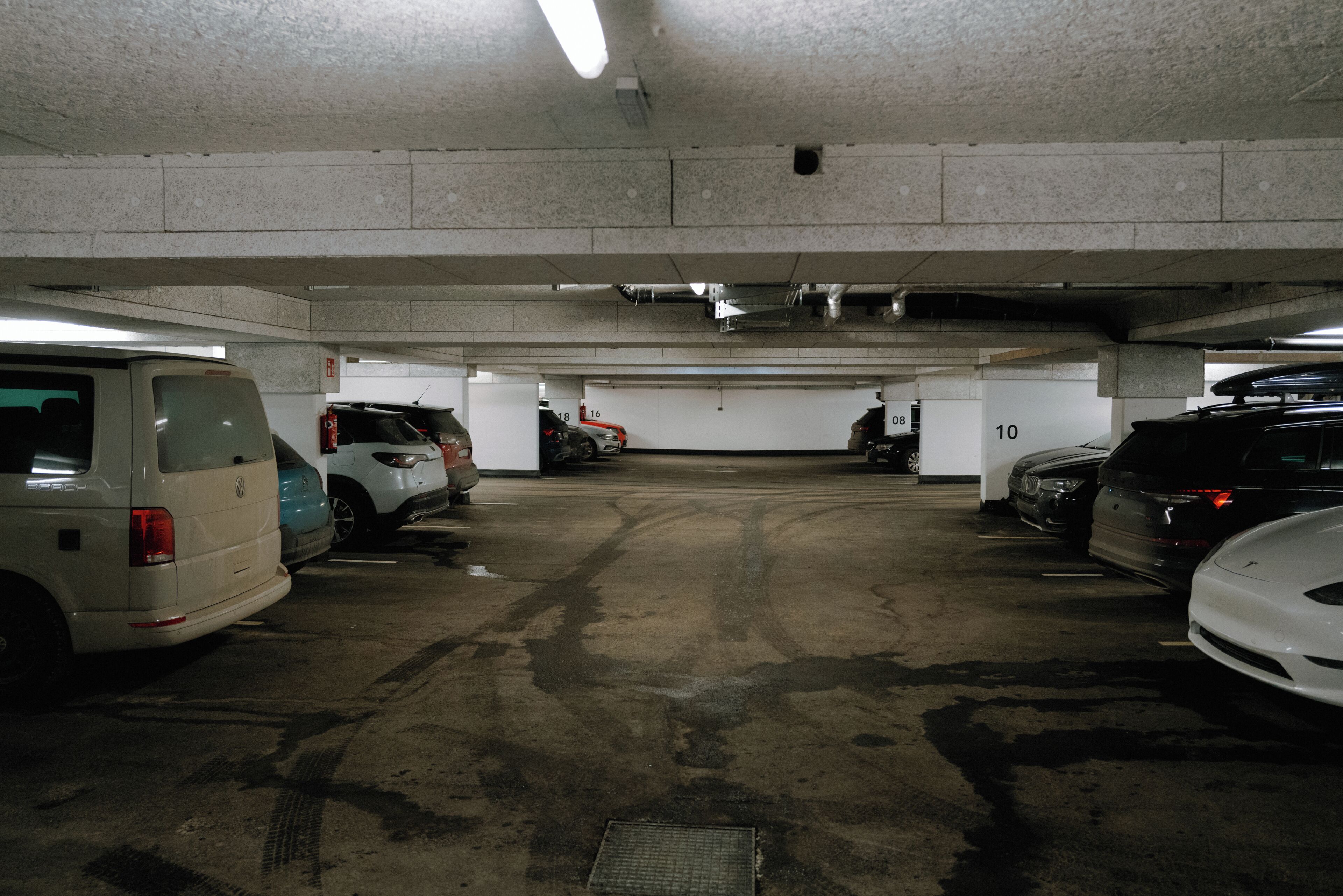 A multi-level underground parking garage with concrete walls and floors, featuring several parked cars and visible parking space numbers.