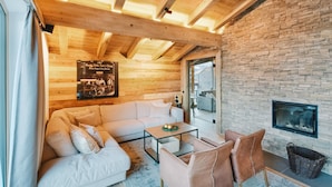 A cozy living room with a wooden ceiling, stone wall, white sofa, and a fireplace. - Venediger Lodge (Neukirchen am Grossvenediger)