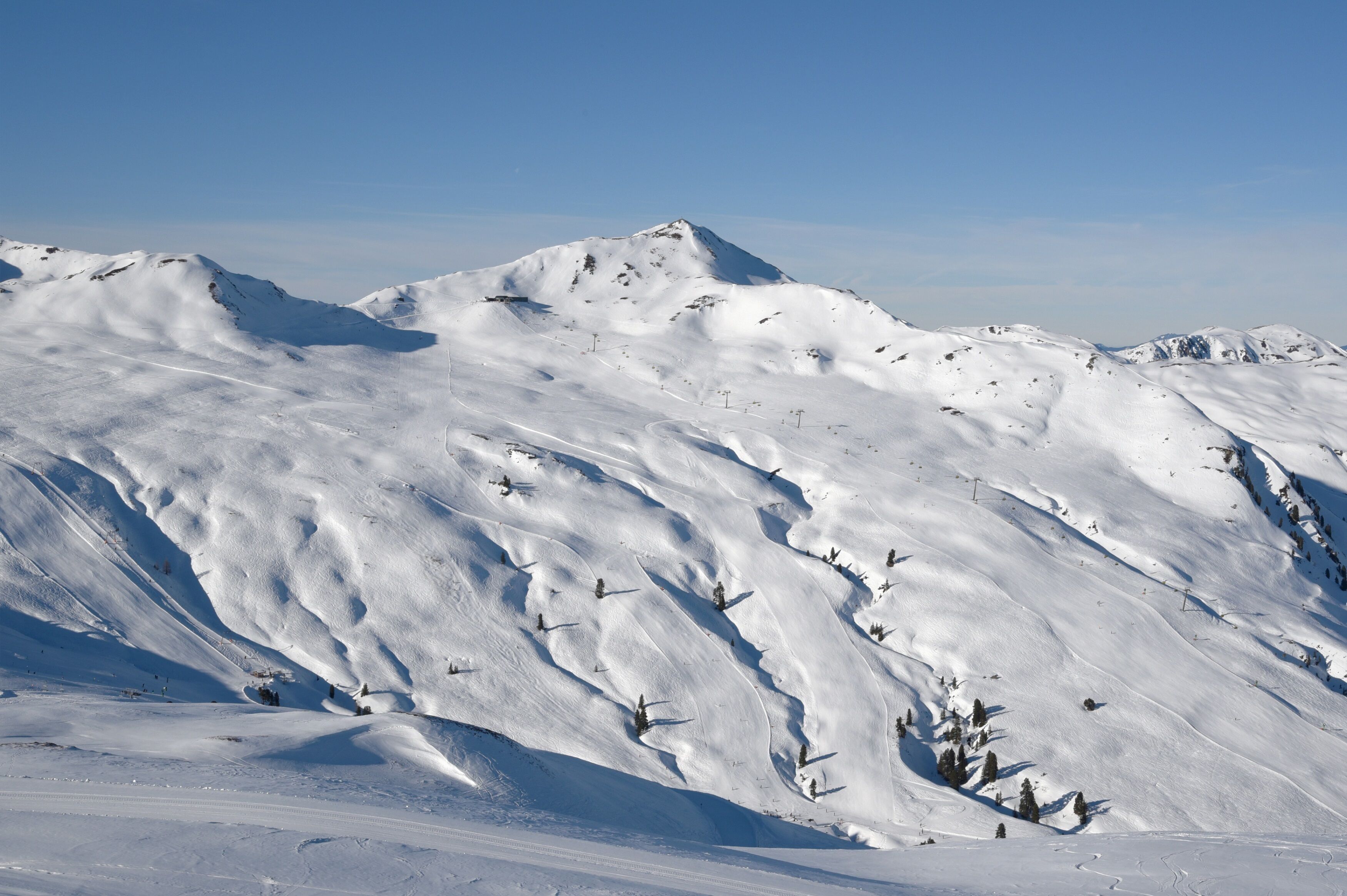 Ein schneebedeckter Berg mit Skiabfahrten und vereinzelten Bäumen.