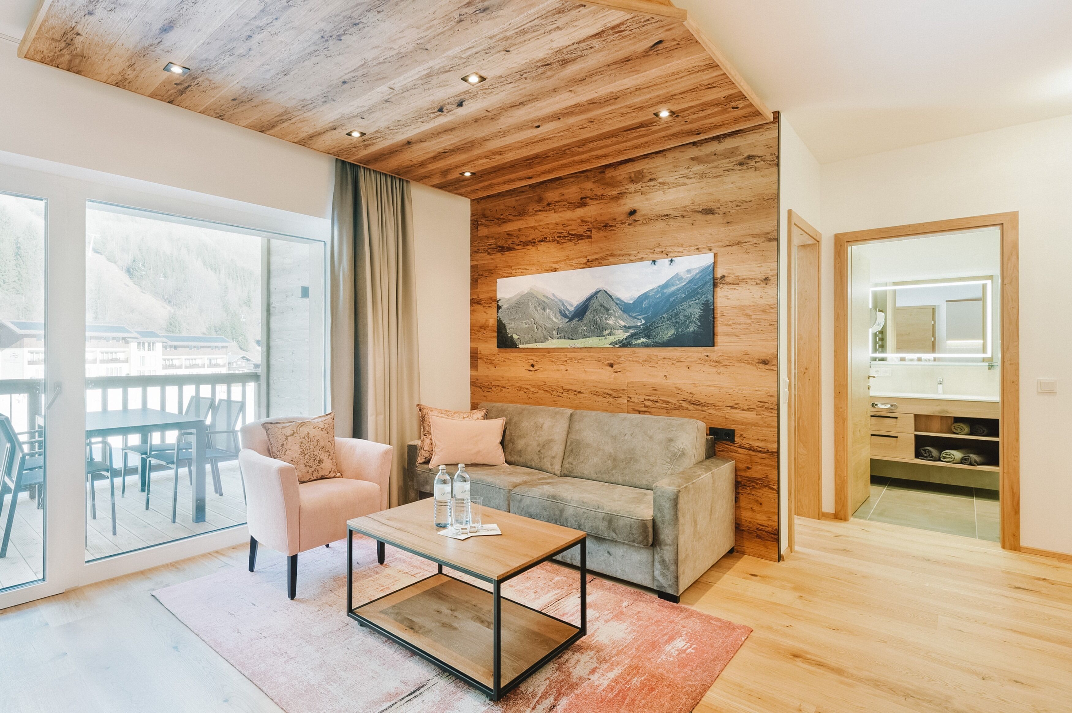 Ein modernes Wohnzimmer mit Holzboden, einem grauen Sofa, einem rosafarbenen Sessel und einem Glastisch.