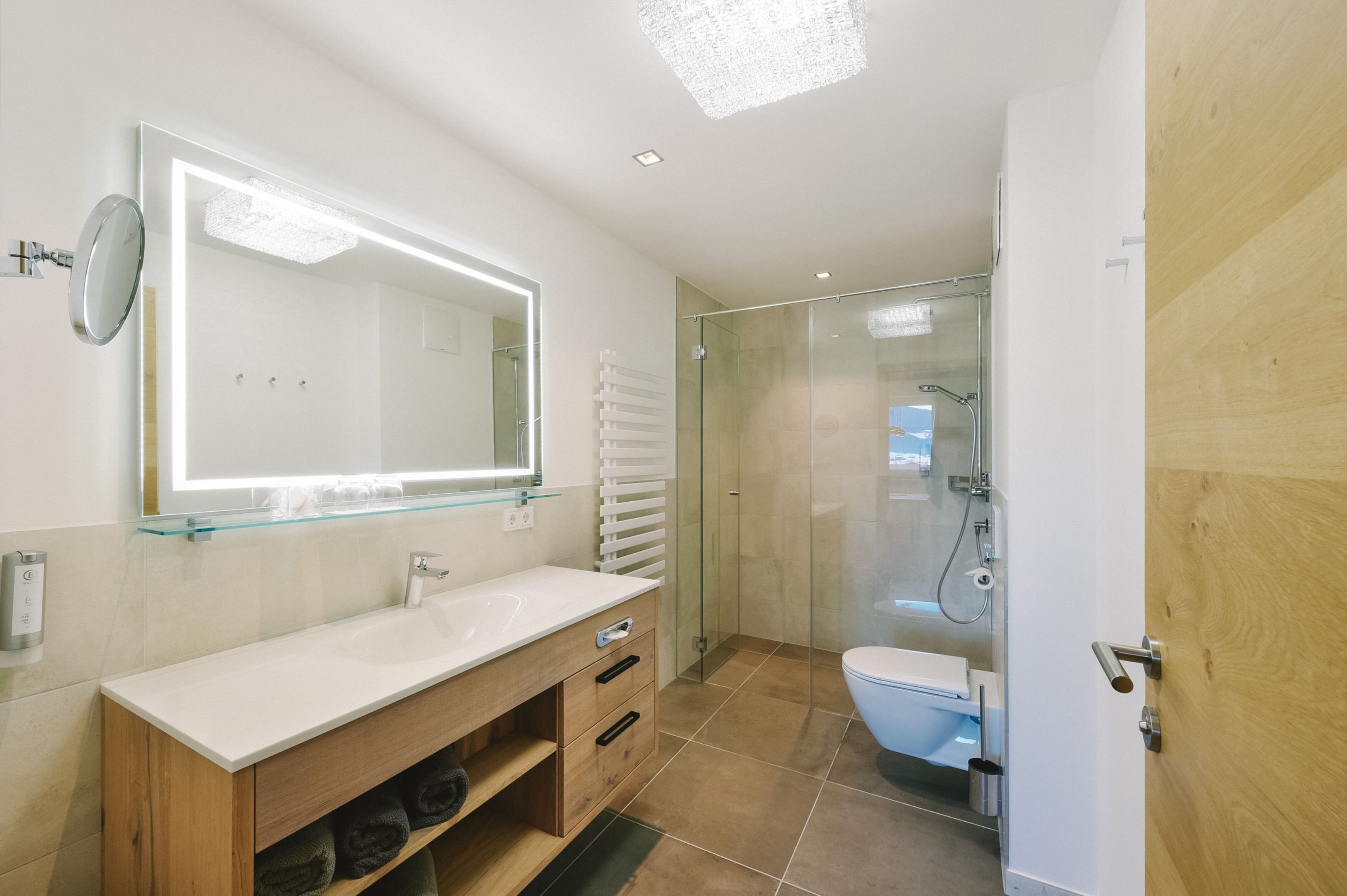 Een moderne badkamer met een douche met glazen wanden, een grote spiegel en een houten wastafelmeubel.