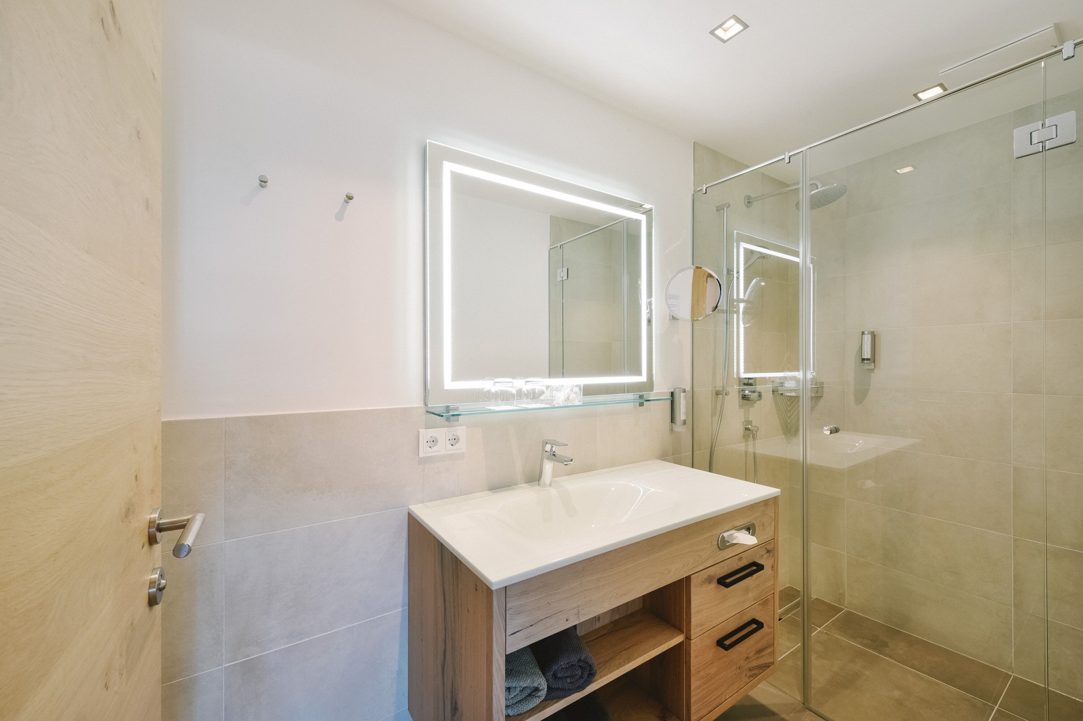 Une salle de bain moderne avec une douche à parois de verre, un lavabo blanc et un meuble-lavabo en bois doté de tiroirs.