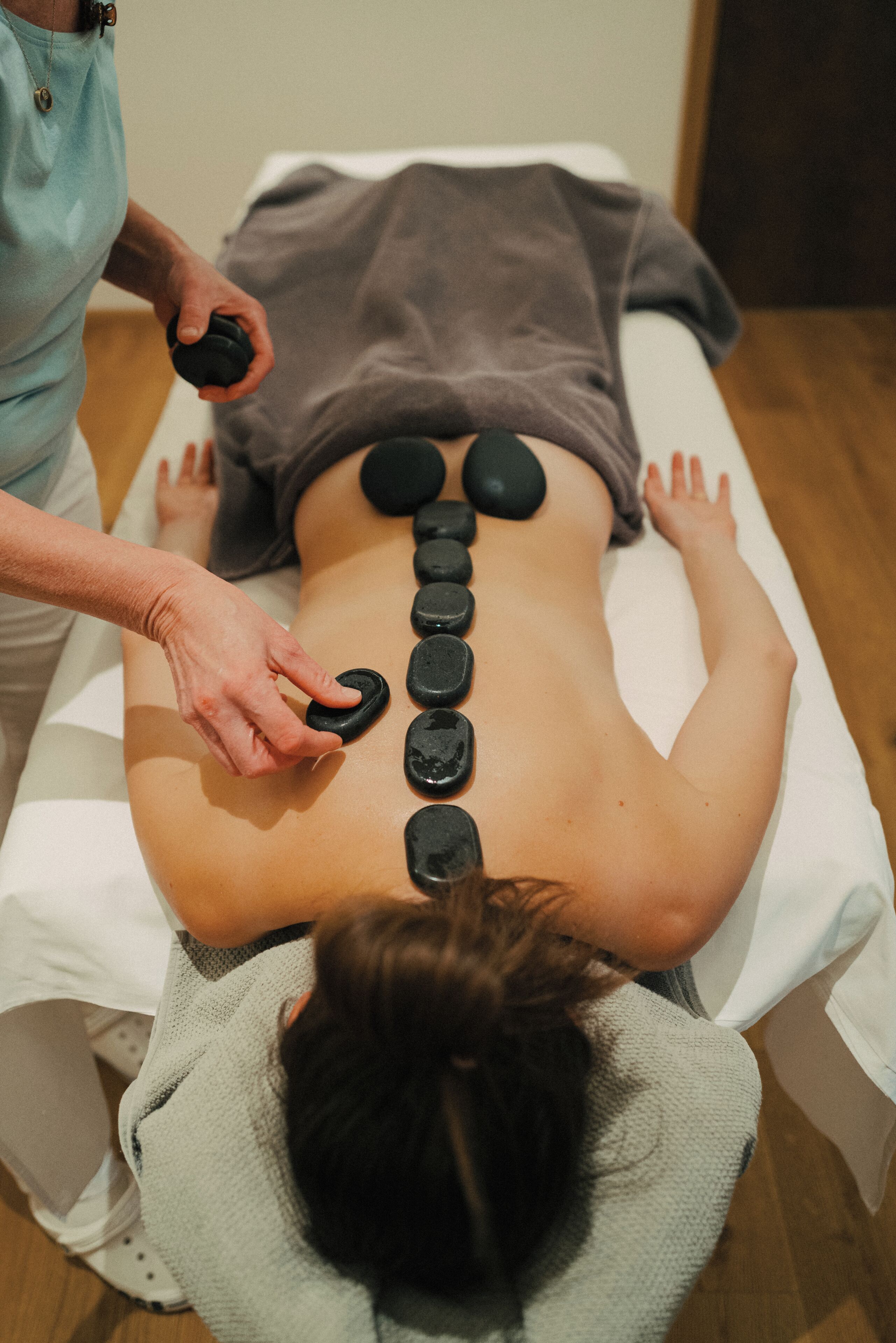 A person receiving a back treatment with multiple black stones placed along their spine.
