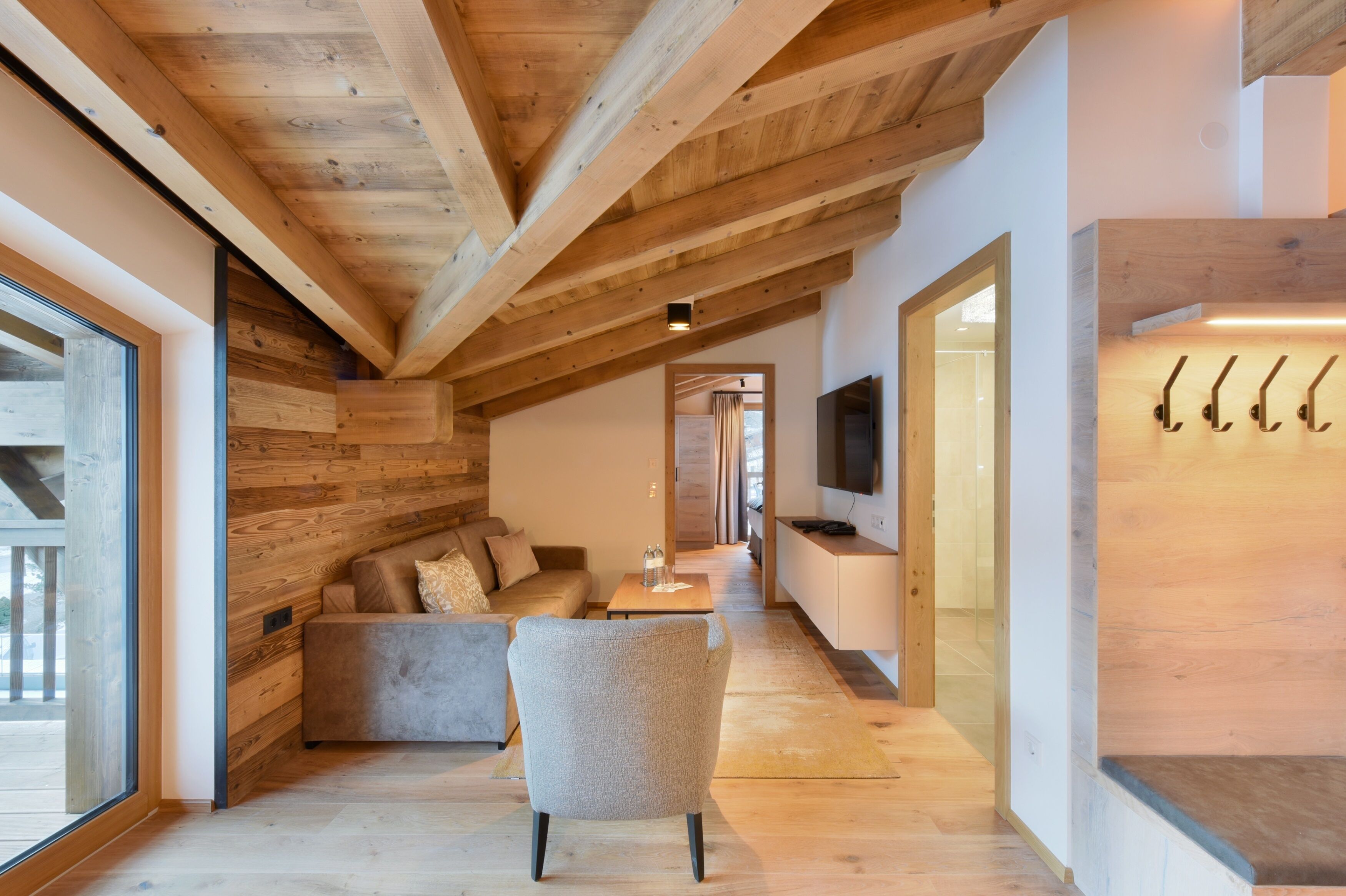 Un intérieur moderne avec des poutres apparentes, un canapé, un fauteuil et un téléviseur fixé au mur.