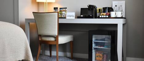 Una camera d'hotel con una scrivania, una sedia, una lampada, una macchina per il caffè, un frigorifero e un letto con coperta.