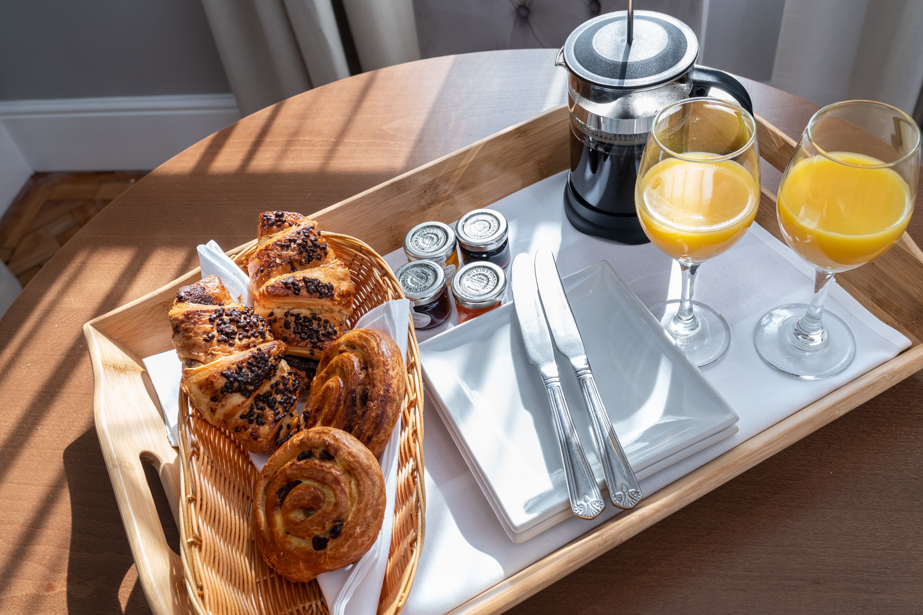A breakfast tray with pastries, condiments, a coffee maker, and glasses of orange juice.