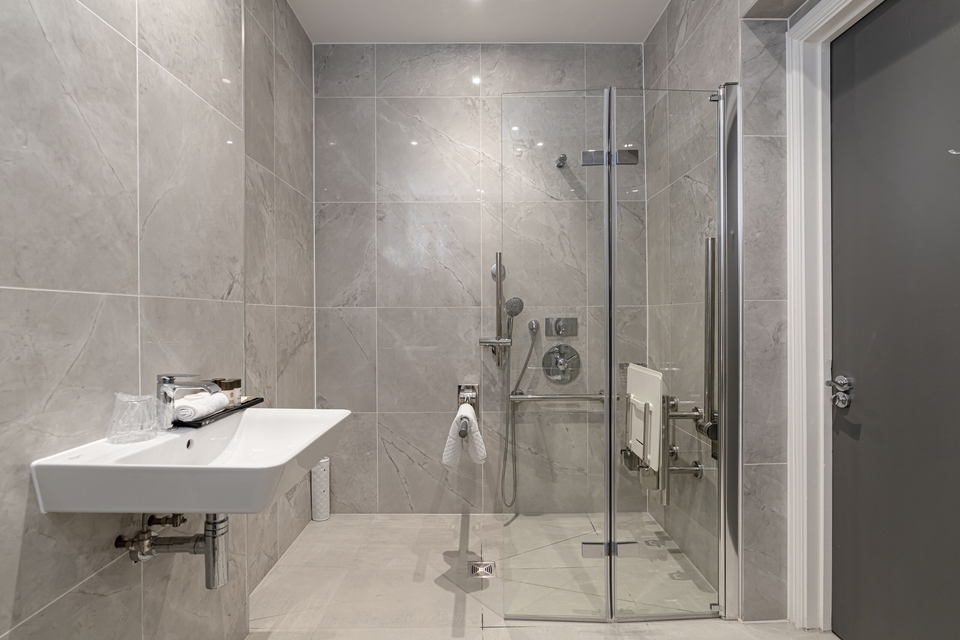 A modern bathroom with a glass-enclosed shower, a white sink, and a towel rack.