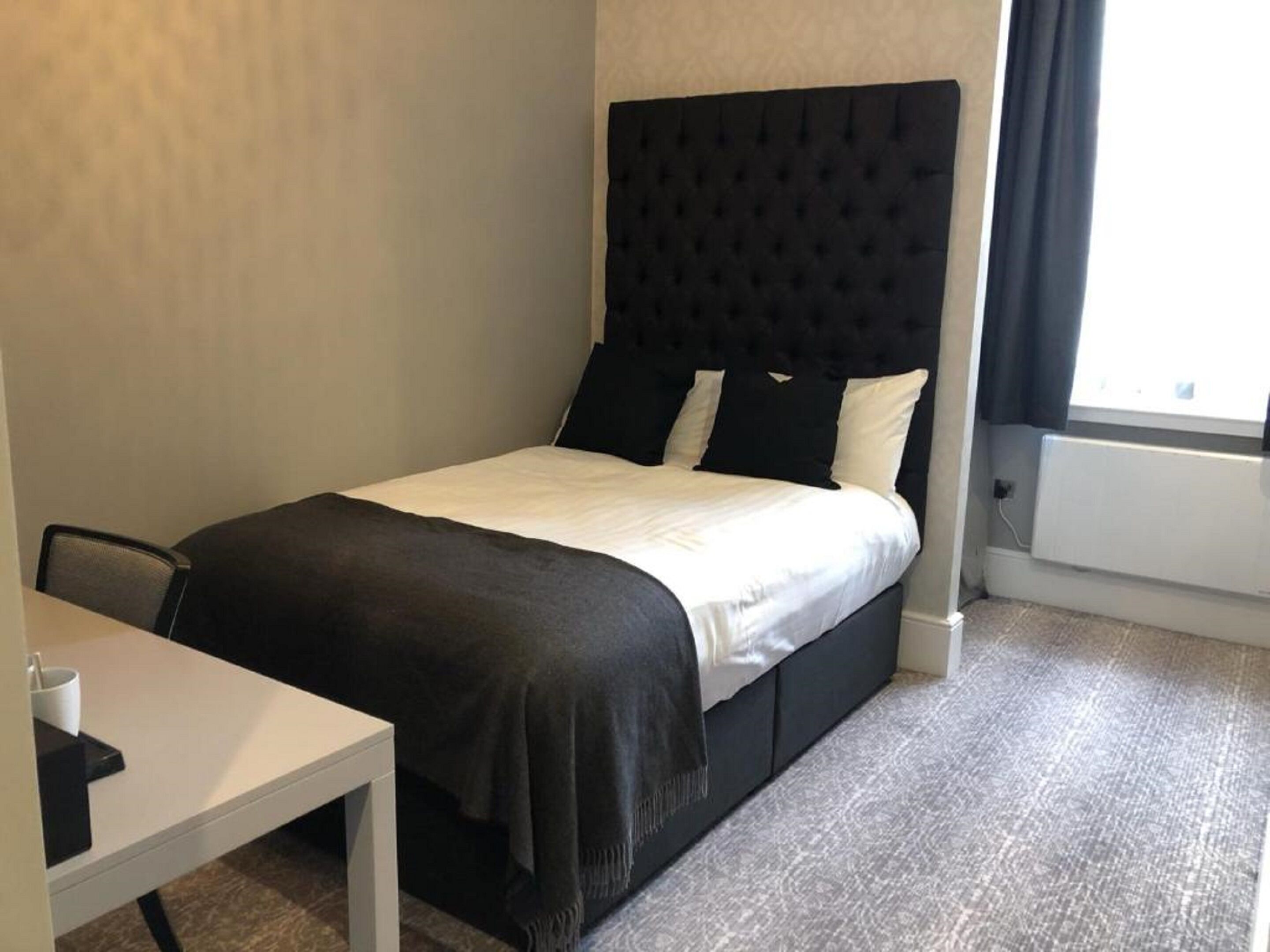 Una habitación de hotel con una cama, una mesita y un ventanal con cortinas.