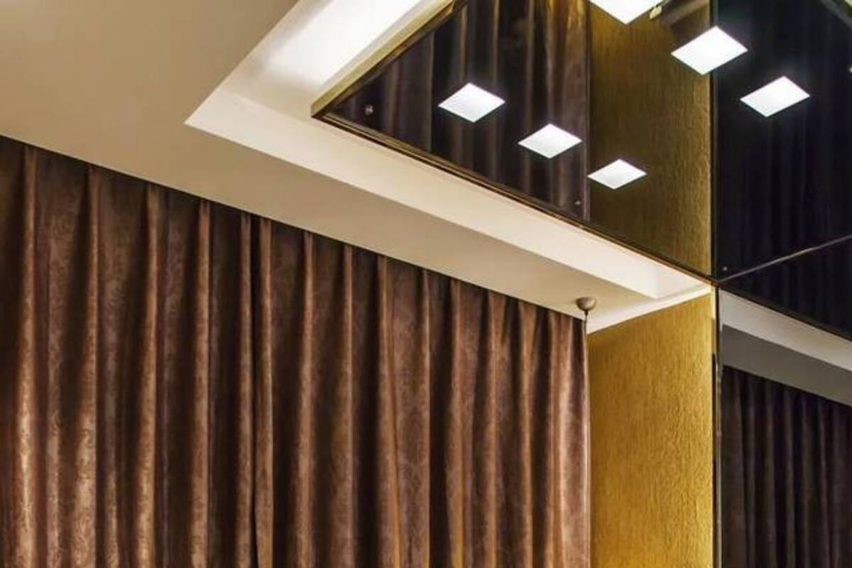 Hotellihuone, jossa on suuri sänky, tummat verhot, sängynpääty, jossa on lamppu, ja kattoon upotetut valaisimet.