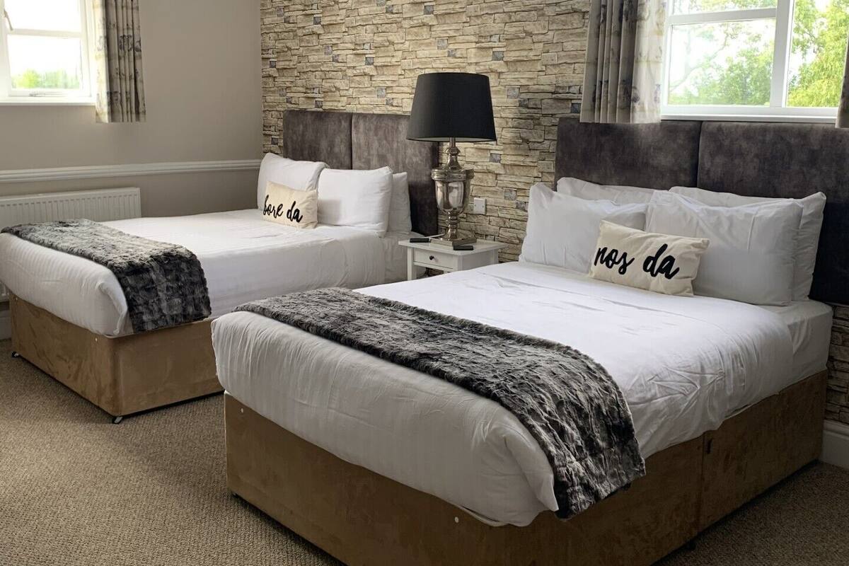 A hotel room with two beds, a stone wall, a window, and a lamp.