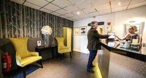 A reception area with a modern design, including a reception desk, chairs, and a wall with a tree pattern. - Faenol Fawr Hotel (Rhyl)