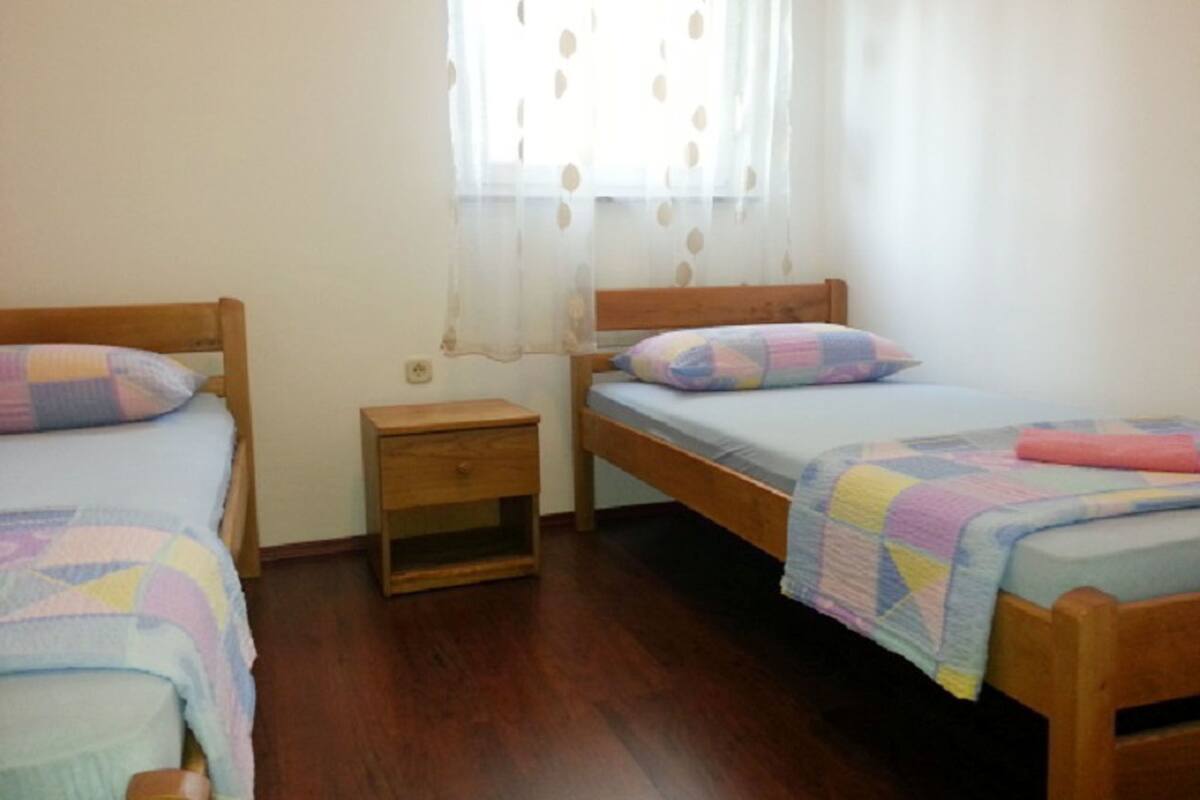 Une chambre avec deux lits en bois, chacun doté d’une tête de lit et d’un pied de lit assortis. Une petite table de chevet en bois se trouve entre les deux lits.