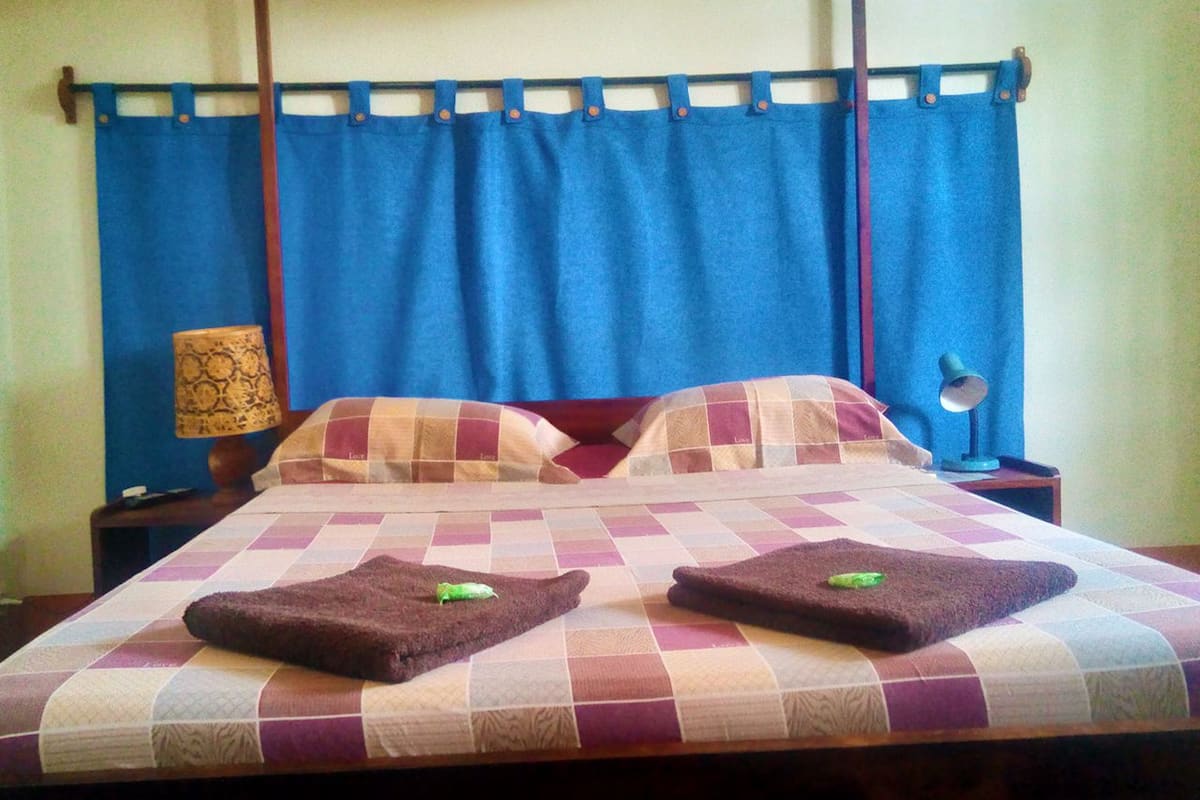 Een bed met een geruit sprei, twee handdoeken en een nachtkastje met een lamp.