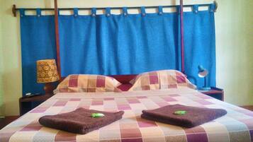 Un letto con copriletto a quadretti, due asciugamani e un comodino con una lampada.