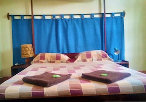 A bed with a checkered bedspread, two towels, and a nightstand with a lamp. - Hotel Le Petit Paradis (Antsiranana)