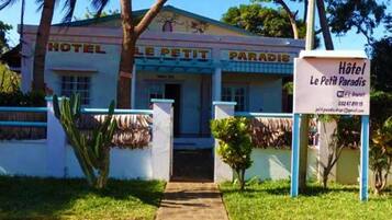 Un hotel chiamato "Le Petit Paradis" con una facciata semplice, un ingresso centrale e un piccolo giardino.