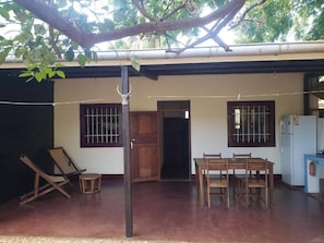 A covered outdoor area with a dining table and chairs, a wooden door, and a window with bars. - Hotel Le Petit Paradis (Antsiranana)