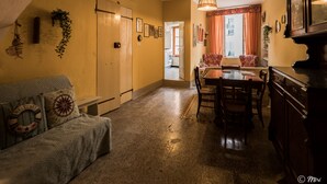 A cozy living room with a sofa, a dining table with chairs, and a kitchen area visible through an open door. - La Casa di Eio Traditional Apartment (Vernazza)