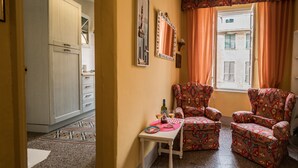 A hotel room with a patterned armchair, a small table with a bottle and glasses, and a view of buildings through the window. - La Casa di Eio Traditional Apartment (Vernazza)