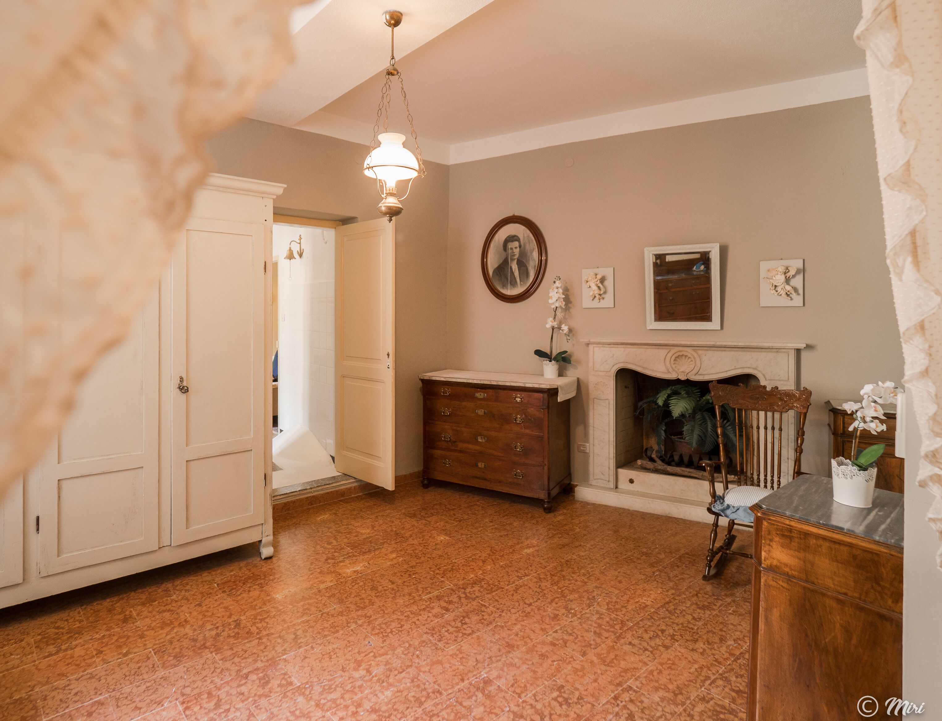 A room with a fireplace, a wooden dresser, a white cabinet, and a door leading to another room.
