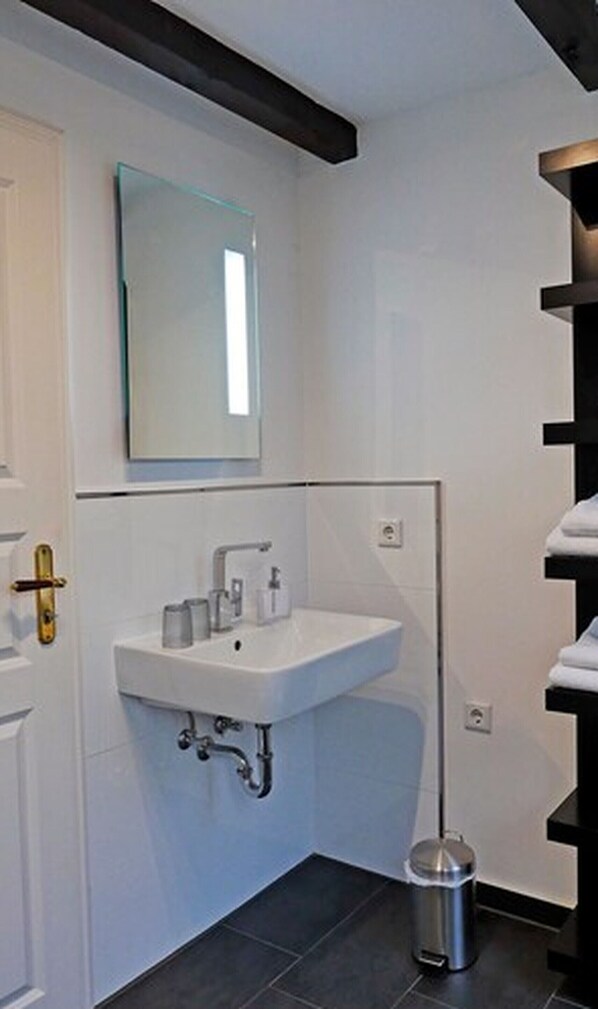 Un baño moderno con lavamanos blanco, espejo y suelo de baldosas negras.