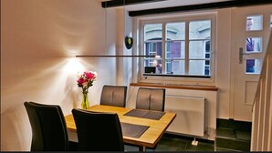 Ein Essbereich mit Tisch, Stühlen, einer Blumenvase und einem Fenster mit Blick auf Gebäude.