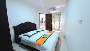 Een hotelkamer met een bed, een klein tafeltje, een raam met gordijnen en een deur naar een balkon.
