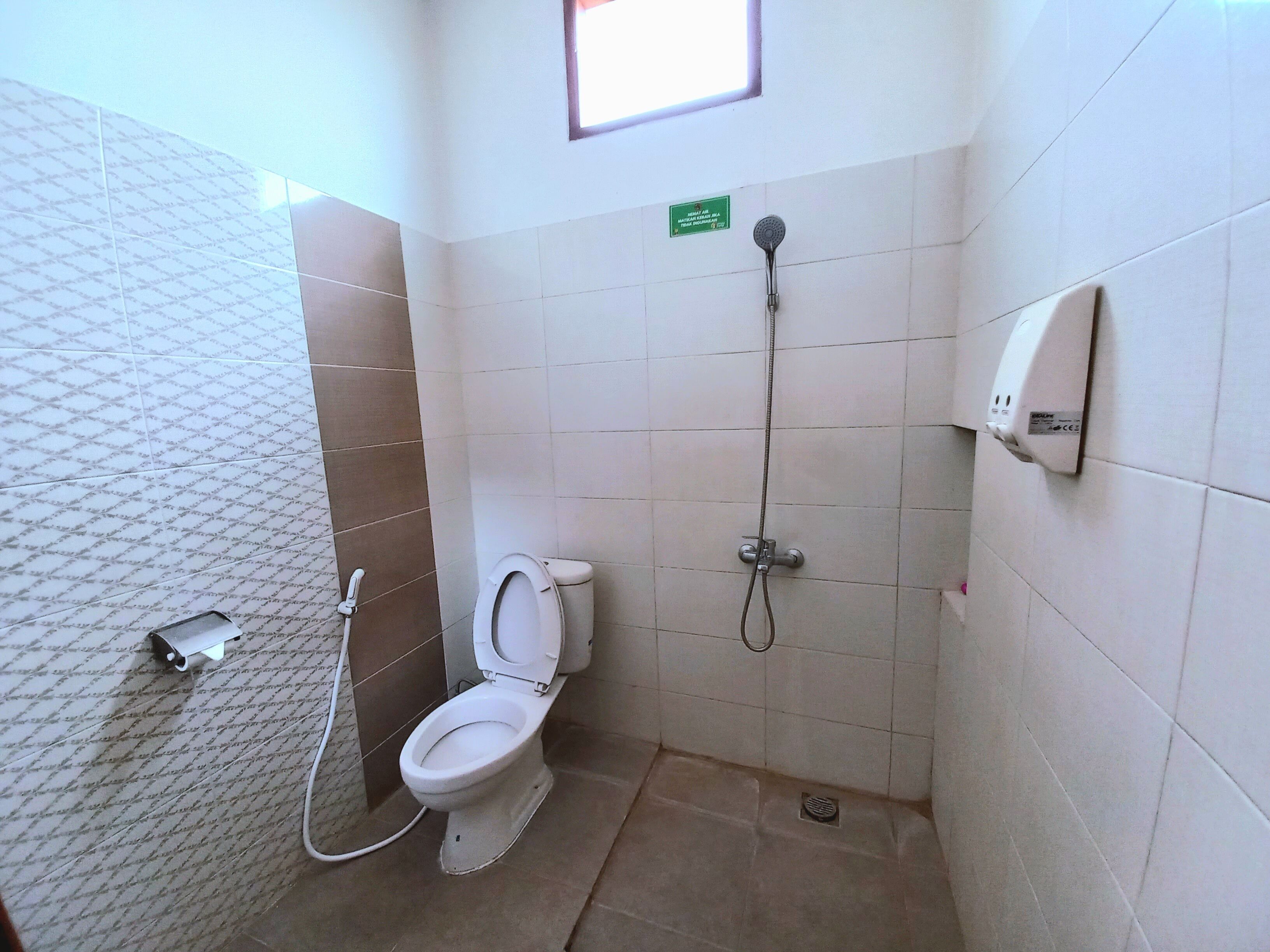 A small, tiled bathroom with a toilet, a shower, and a hand dryer.