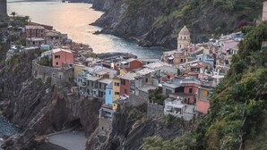 Un village côtier aux bâtiments aux couleurs vives, adossé à des falaises rocheuses qui surplombent la mer.
