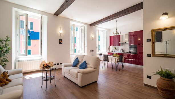Un salon spacieux avec un canapé et des fauteuils, un coin repas avec une table et des chaises, et une cuisine avec des meubles rouges et un lustre.