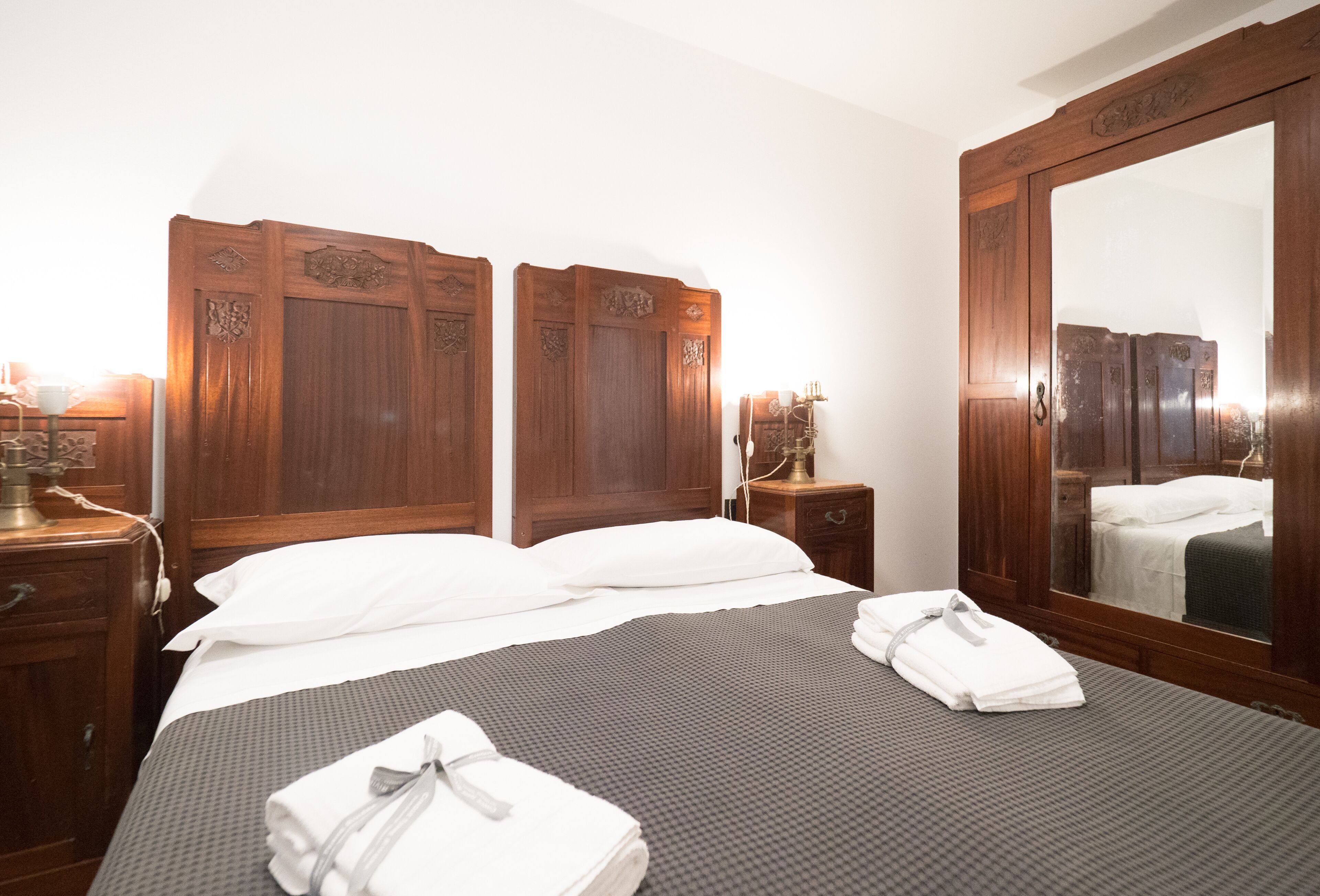 Habitación de hotel con una cama grande, cabecero de madera, un espejo y una mesita de noche con una lámpara.