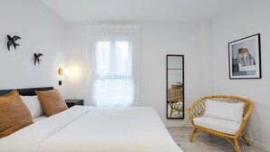 A bedroom with a large bed, a wicker chair, a mirror, and wall art. - Mad Apartments by Olala Homes (Madrid)
