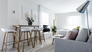A modern living room with a grey sofa, a coffee table, and a TV. There are two white chairs with wooden legs and a small table with a potted plant. - Mad Apartments by Olala Homes (Madrid)