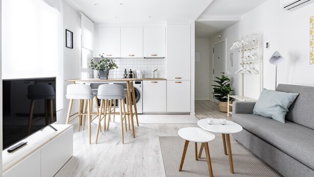 A modern kitchen with white cabinets, a dining area with a white table and chairs, and a grey sofa with a light blue pillow. - Mad Apartments by Olala Homes (Madrid)